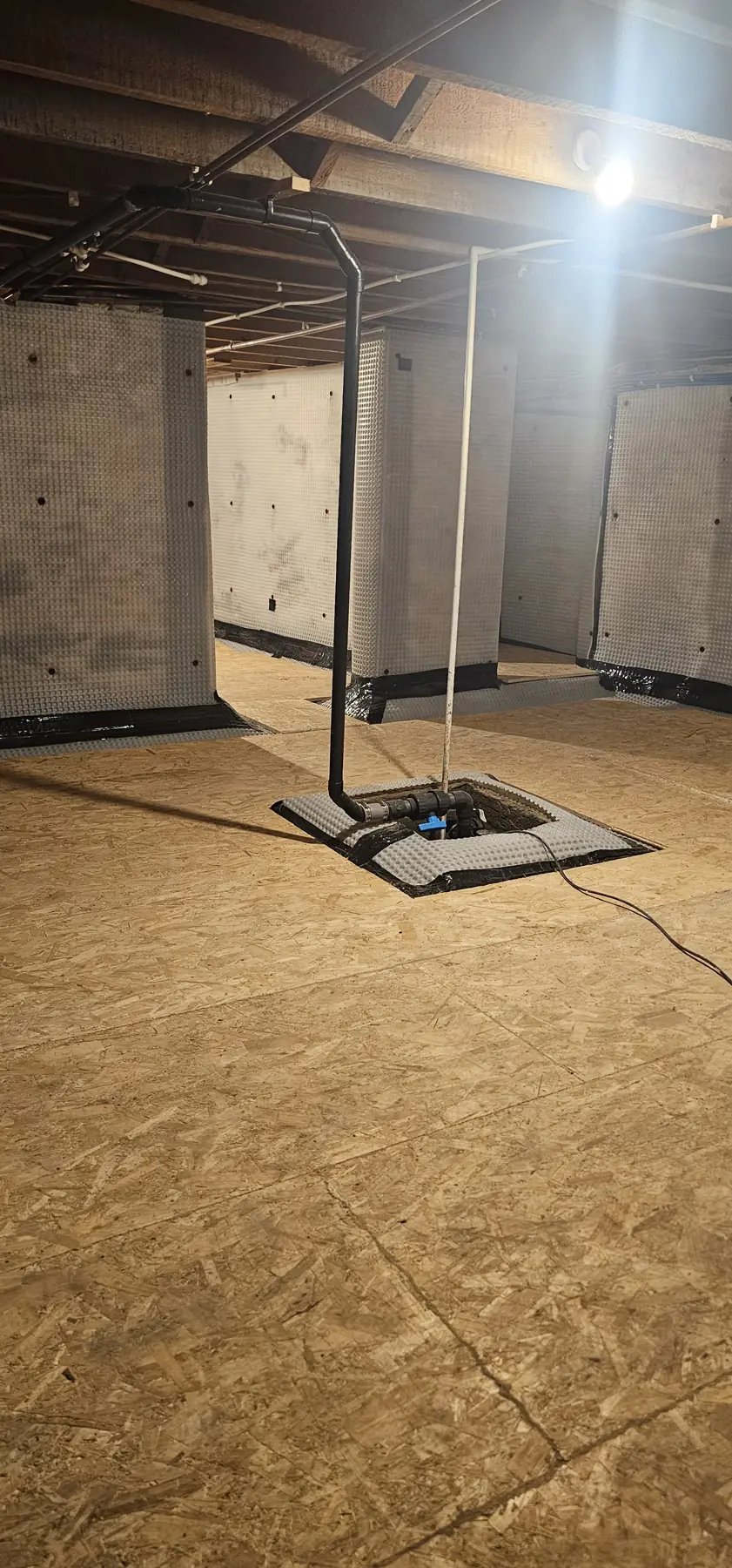 New sump and pump set into the boarded basement floor with the discharge pipe running up to the ceiling