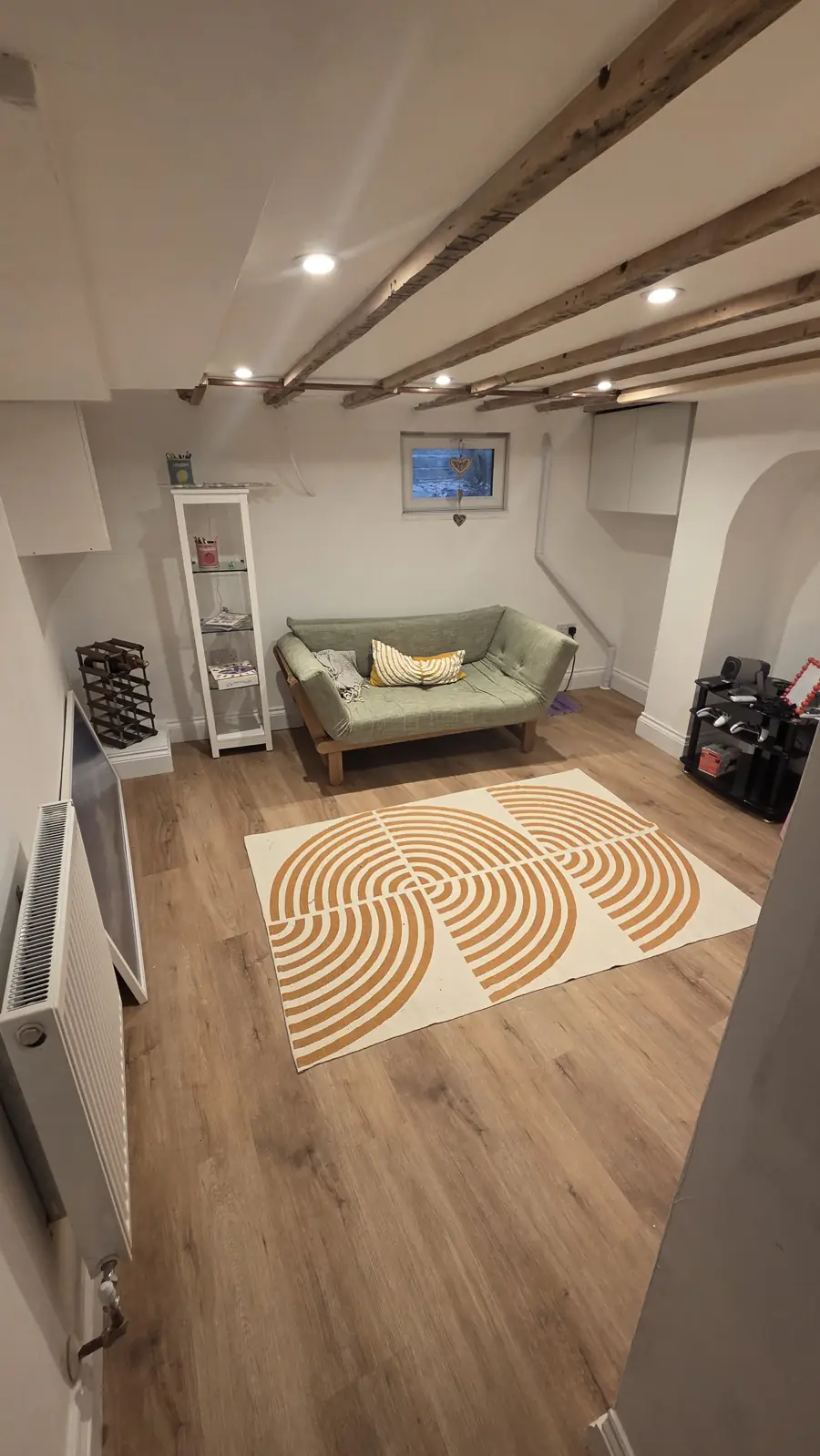 Converted cellar in Faversham with exposed oak beams, oak flooring, a green sofa and a small window