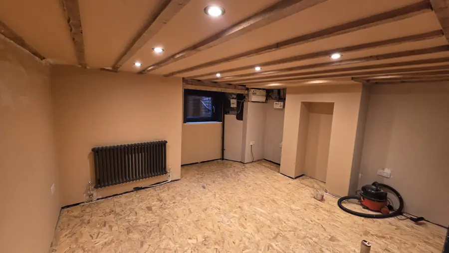 Converted cellar with exposed beams, column radiator, new window and freshly plastered walls, ready for flooring