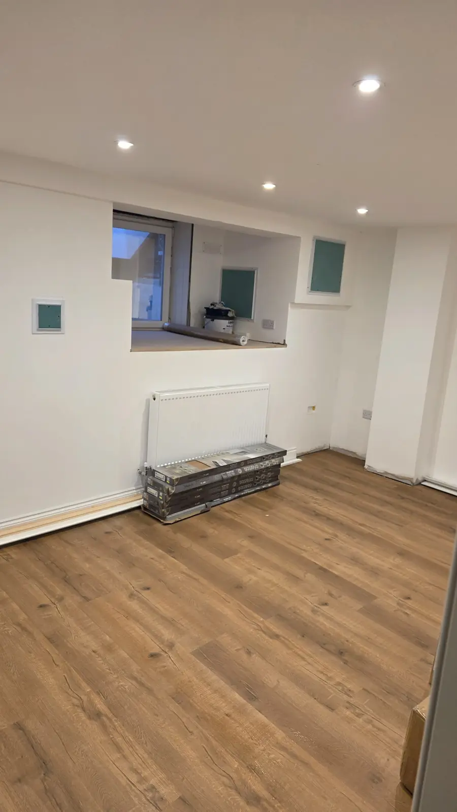 After: finished basement bedroom in Maidstone with white walls, downlights, oak-effect floor, radiator and a large window