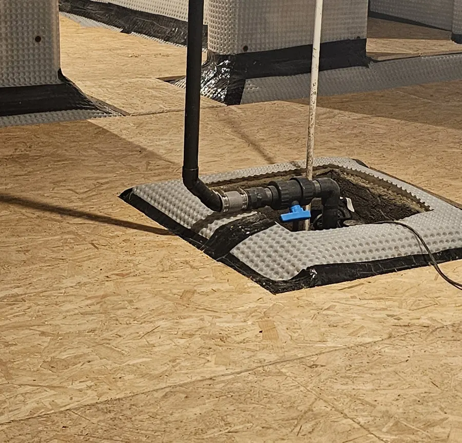 Close-up of a sump pump set into a boarded basement floor, with the discharge pipe and non-return valve, installed by Lark Basements